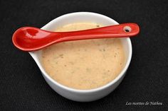 a red spoon sitting in a white bowl filled with dip and cheese sauce on a black surface