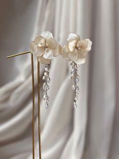 two white flowers are hanging from the side of a pair of gold ear pins on a stand