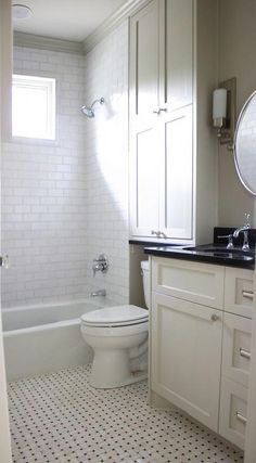 a white toilet sitting next to a bath tub in a bathroom under a window on top of a tiled floor