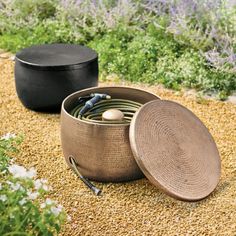 two round baskets sitting on top of a gravel ground next to plants and flowers in the background