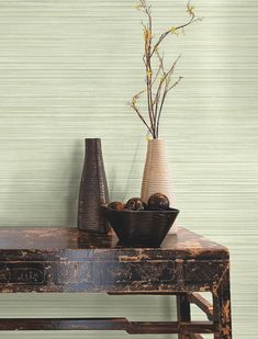 two vases and a bowl on a table with a wallpapered background behind it