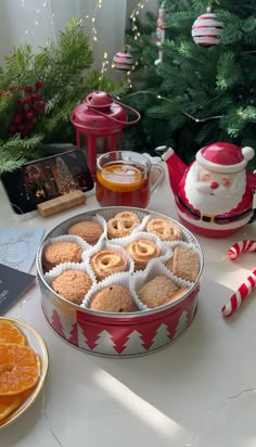 an assortment of cookies and oranges on a table next to a christmas tree with decorations