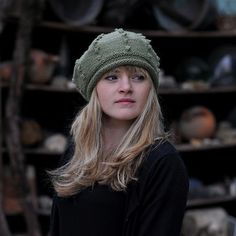 a woman wearing a green knitted hat in front of a rack of pots and pans