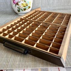 a wooden tray with many compartments on top of a table next to a vase and flower pot