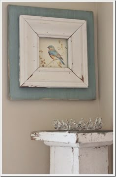 a blue and white bird sitting on top of a mantle next to a framed painting