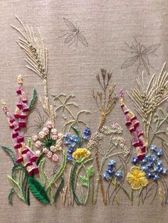 some flowers and grass are embroidered onto a piece of cloth with thread on it,