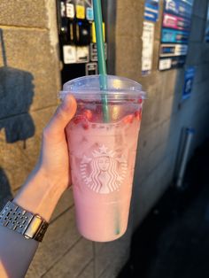 a person holding up a pink drink in front of a vending machine