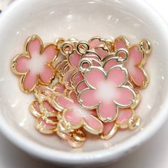 Qty x 1 Charm Light gold plated flower charms with pink and white translucent enamel as pictured.  Approximate Measurements: 18mm x 15mm x 1.2mm with a 2mm hole Pink Enamel Jewelry With Flower Charm, Pink Enamel Flower-shaped Jewelry, Pink Flower Pendant Jewelry With Charms, Cute Pink Flower Pendant Jewelry, Pink Enamel Charms Jewelry, Pink Enamel Jewelry With Charms, Gold Flower Charm For Jewelry Making, Gold Jewelry With 3d Flowers For Jewelry Making, Pink Enamel Charms For Gifts