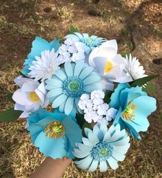 a bouquet of blue and white flowers in someone's hand with grass behind it