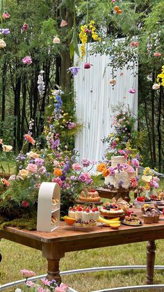 an outdoor table with flowers and cakes on it