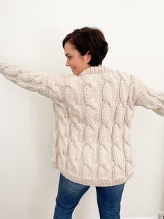 a woman in a white sweater is holding her arms out to the side while standing against a wall