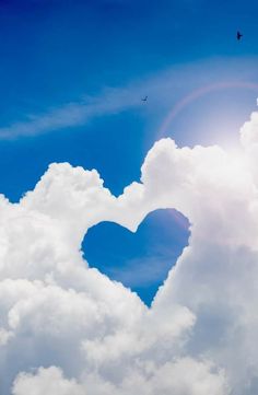 a heart shaped cloud in the sky with a bird flying above it and a bright blue sky