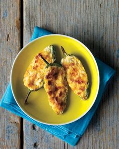 two stuffed peppers on a yellow plate next to a blue napkin and fork, sitting on a wooden table