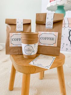 two coffee bags sitting on top of a wooden stool next to a cup and paper bag