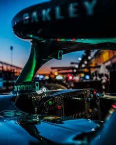 the front end of a blue sports car with lights on at night and bridge in background