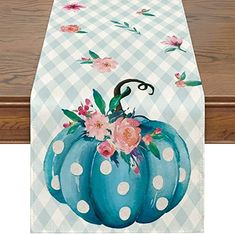 a blue pumpkin decorated with pink flowers on a checkered table cloth, hanging from a wooden rail