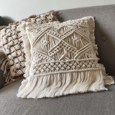 two pillows on a couch with fringes and tassels in the back ground