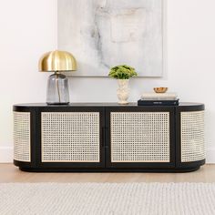 a black and white sideboard with a gold lamp on top next to a painting