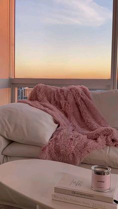 a pink blanket sitting on top of a white couch next to a book and cup