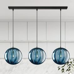 three blue glass globes hanging from a black metal bar with white marble walls in the background