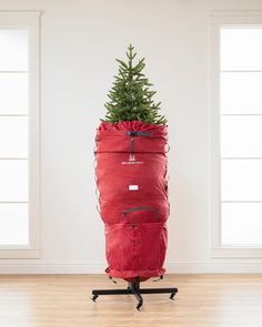 a christmas tree is placed in a red bag on a black stand and it's attached to the wall