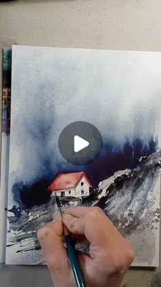 a person is holding a pencil in their hand and painting a house on a canvas