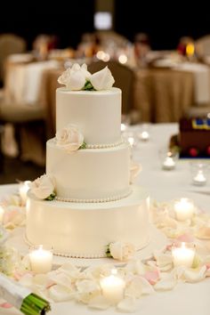 a three tiered white wedding cake with flowers and candles on the table at a reception