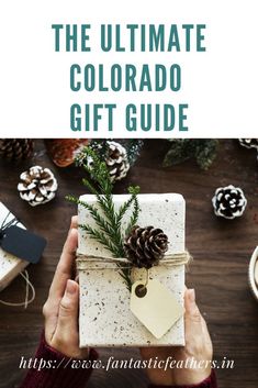 someone holding a gift wrapped in white paper with pine cones on top and the words, the ultimate colorado gift guide