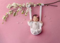 a baby is laying down on a swing with white flowers hanging from it's side