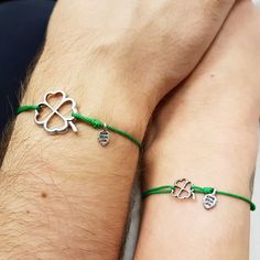 two people wearing green string bracelets with silver charms on their wrists, one holding the other's hand