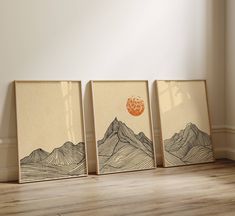 three framed art prints with mountains and an orange sun in the middle on a wood floor