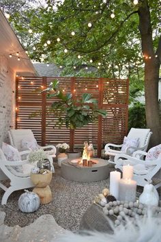 an outdoor fire pit surrounded by white chairs and trees with lights strung over the top