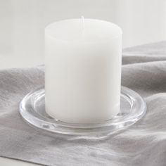 a white candle sitting on top of a glass plate next to a gray linen napkin