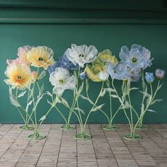 five glass vases with flowers in them on a tile floor next to a green wall