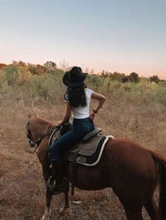 a woman riding on the back of a brown horse in a field with tall grass