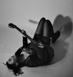 a woman laying on the ground with a guitar in her hand and wearing black tights