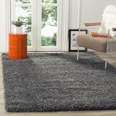 a living room with an orange vase on the floor and a gray rug in front of it