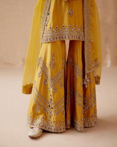 Editor's Note Introducing a stunning mustard kurta sharara adorned with intricate gold floral thread embroidery, elegantly highlighted with various embellishments. This captivating ensemble is paired with an embroidered dupatta, creating a luxurious and regal look perfect for special occasions or festive gatherings. The combination of the rich mustard color, the gold accents, and the ornate embroidery on both the kurta sharara and dupatta adds a touch of opulence, making this outfit a statement Mustard Colour Combination, Sharara Suit Designs, Long Skirt Top Designs, Floral Thread Embroidery, Embroidery Kurta, Sharara Designs, Mom Daughter Outfits, Kurta Sharara Set, Haldi Outfit