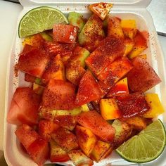 a plastic container filled with watermelon, lime and pineapple slices covered in seasoning