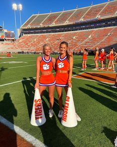 two cheerleaders in orange and blue uniforms holding white cones on a football field