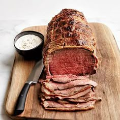 a large piece of meat is on a cutting board with a knife and some sauce