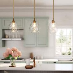 a kitchen with three lights hanging from the ceiling and flowers in vases on the counter