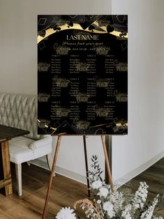 a black and gold wedding seating chart on a easel with flowers in the foreground