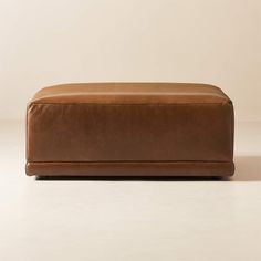 a large brown leather ottoman sitting on top of a white floor next to a wall