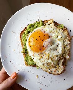 an egg and avocado toast on a white plate with a hand holding it