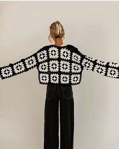 a woman standing in front of a white wall wearing black and white knitted sweater