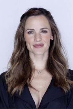 a woman with long brown hair wearing a black shirt and smiling at the camera while standing in front of a white background