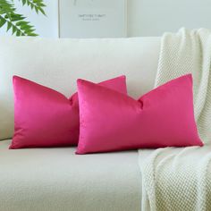 two pink pillows sitting on top of a white couch next to a green leafy plant