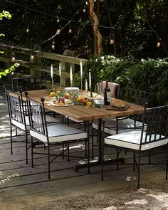 an outdoor dining table with white chairs and lights strung from the trees in the background