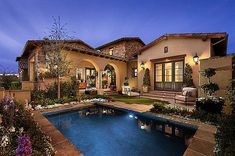 a house with a swimming pool in the front yard and landscaping around it at night